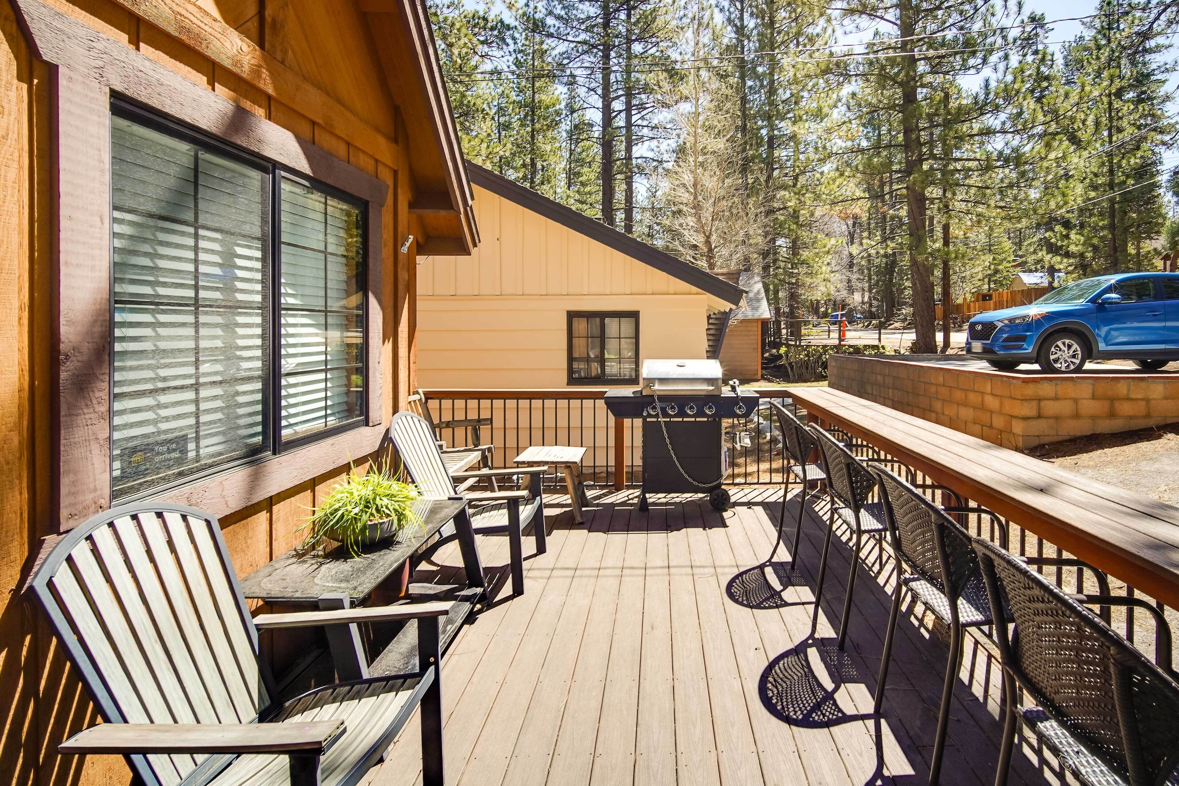 Une terrasse en bois avec des sièges d’extérieur, un barbecue et un véhicule garé à proximité.