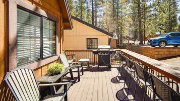 A wooden deck with outdoor seating, a barbecue grill, and a vehicle parked nearby.