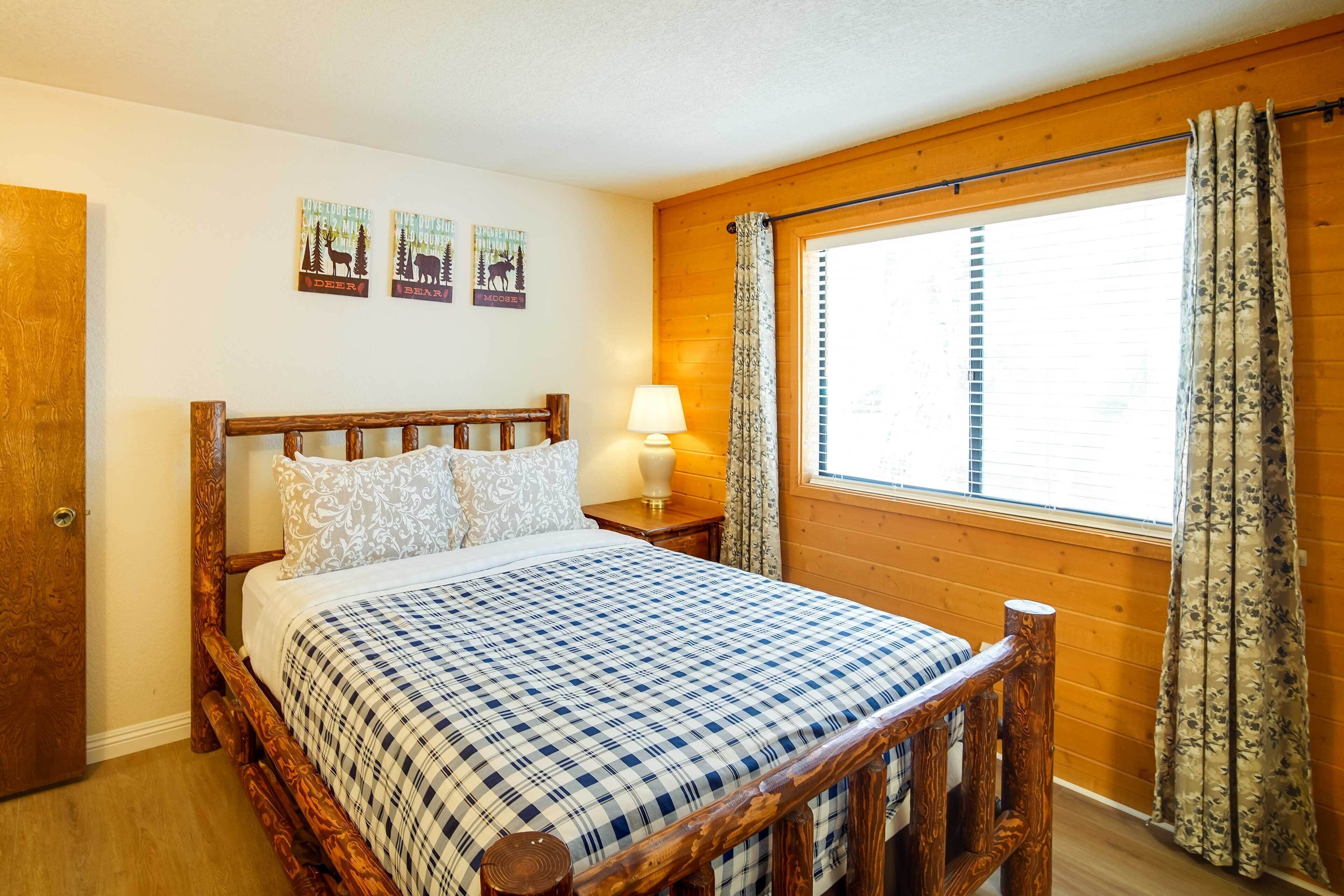 Un lit en bois avec un couvre-lit à carreaux, une lampe de chevet et une fenêtre avec des rideaux.