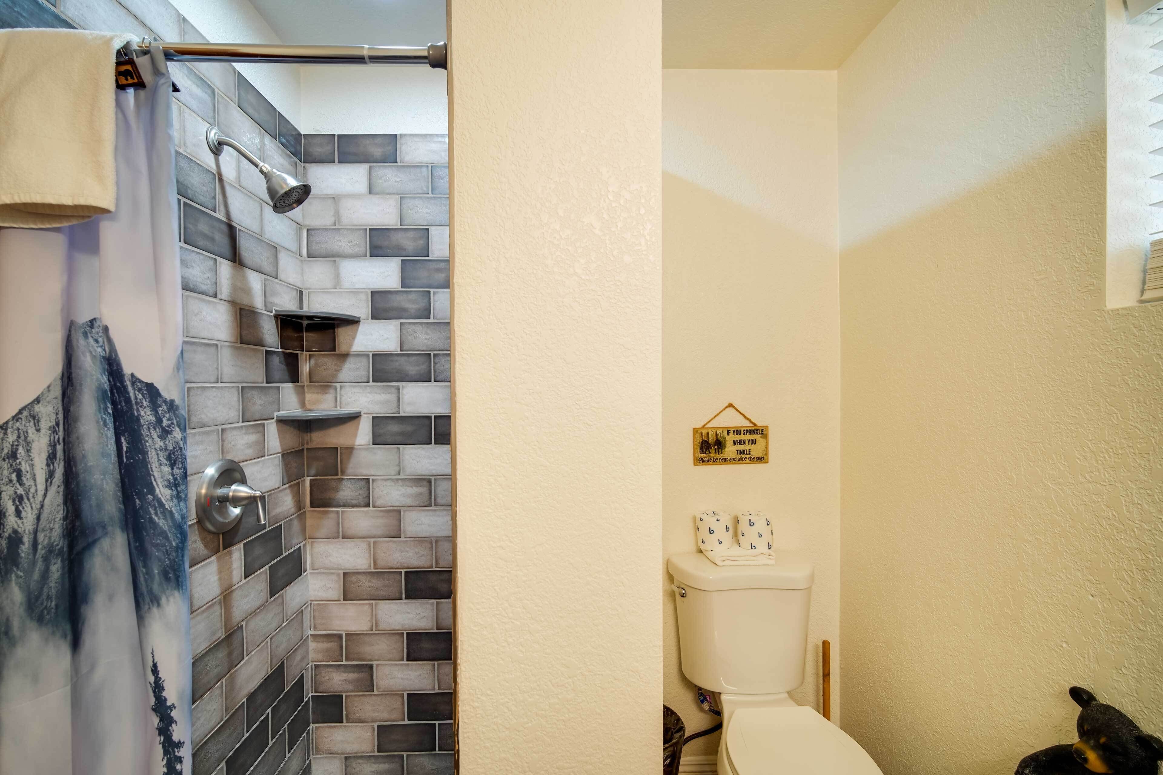 A bathroom with a shower area featuring a tiled wall and a toilet with a bear decoration.