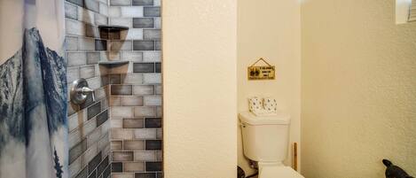 Un baño con zona de ducha, pared azulejada y un inodoro decorado con un oso.