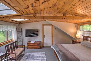 A cozy attic bedroom with a sloped ceiling, a wooden bed, a desk with a chair, a dresser, and a TV mounted on the wall. - Spectacular Views w/ Deck, Fire Pit, & Game Room! (Keuka Park)