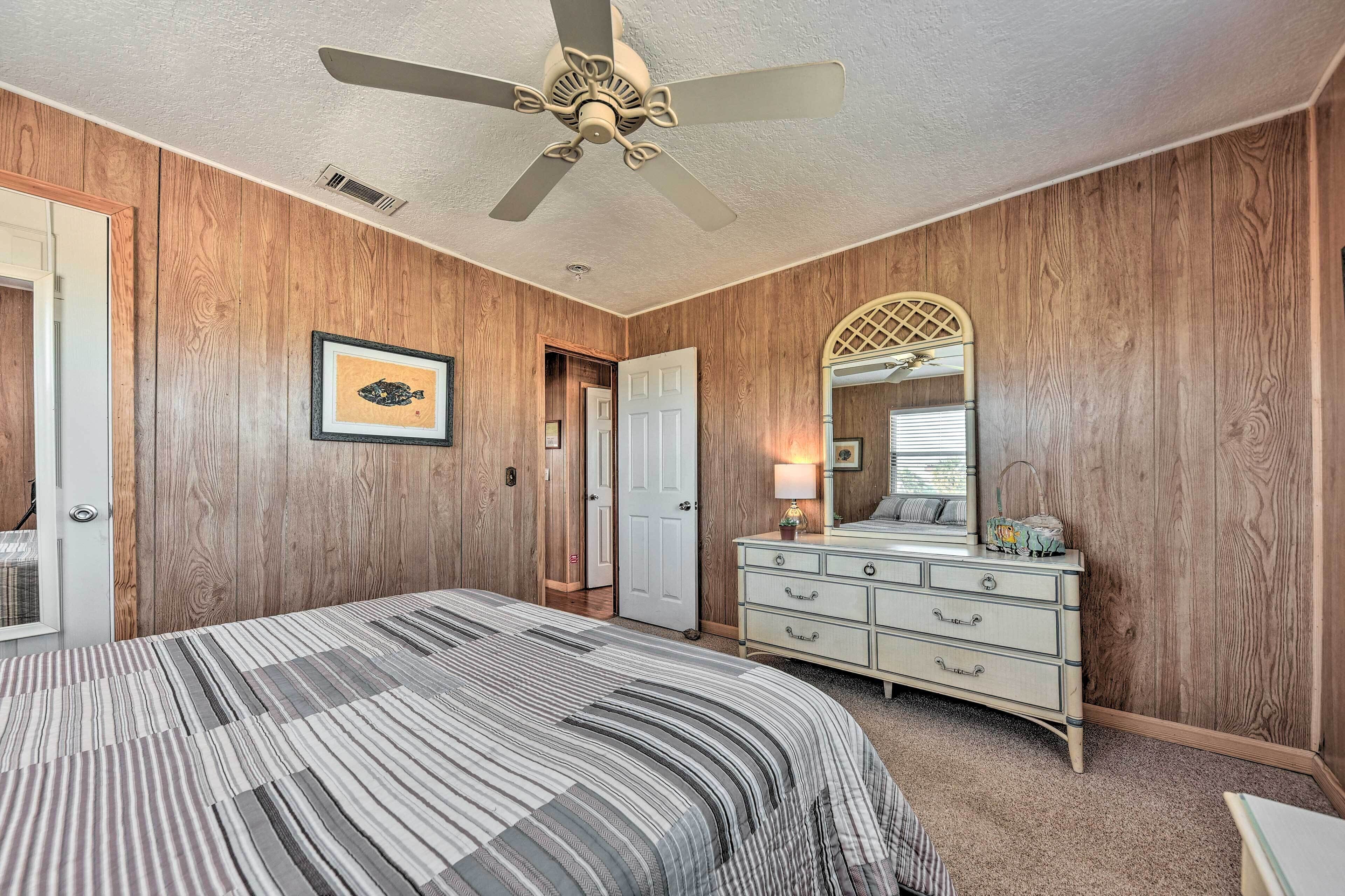 A bedroom with a bed, dresser, ceiling fan, and wooden walls.