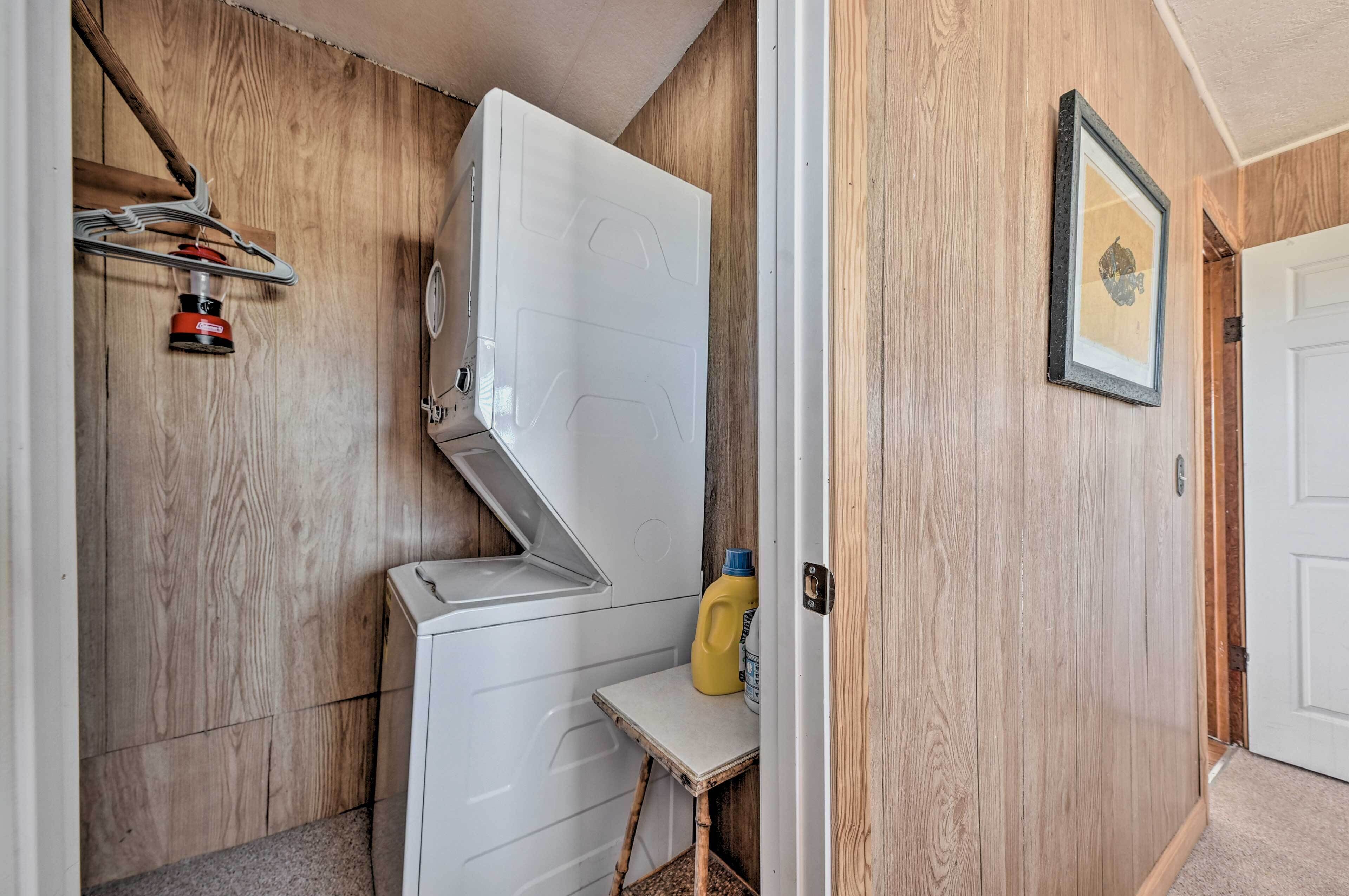 A compact room with a wooden wall, a white washing machine, a small table with a yellow bottle, and a framed picture on the wall.