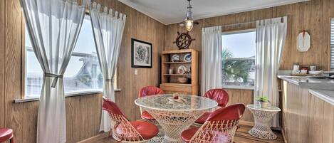 A dining area with a round table and red chairs, wooden walls, and a view through large windows.