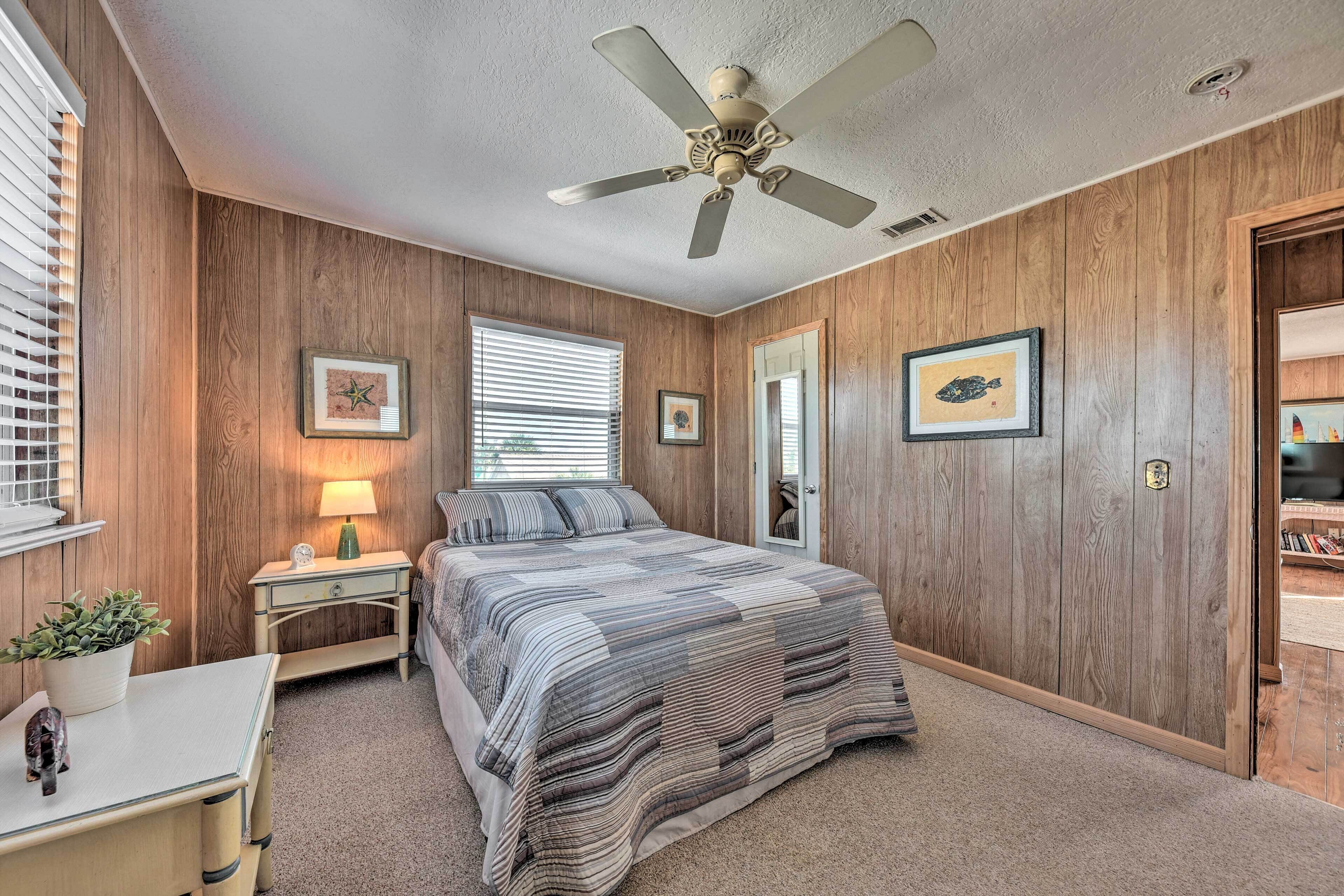 Un dormitorio con cama, mesita de noche, escritorio, ventilador de techo y paredes de madera.