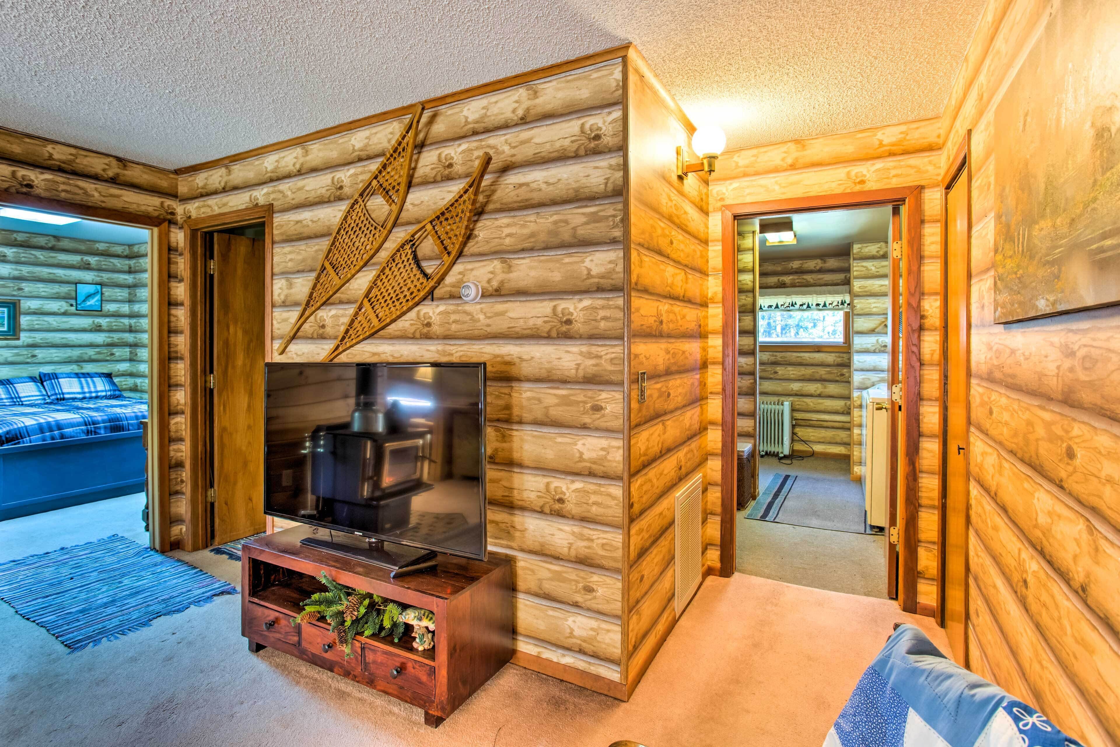 A log cabin interior with a television, wooden walls, a bed, and a dining area.