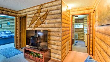 A log cabin interior with a television, wooden walls, a bed, and a dining area.