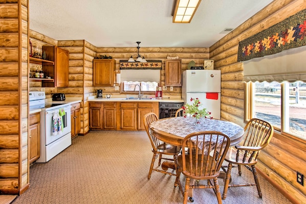 A log cabin kitchen with wooden cabinets, a white refrigerator, a stove, and a dining table with chairs.