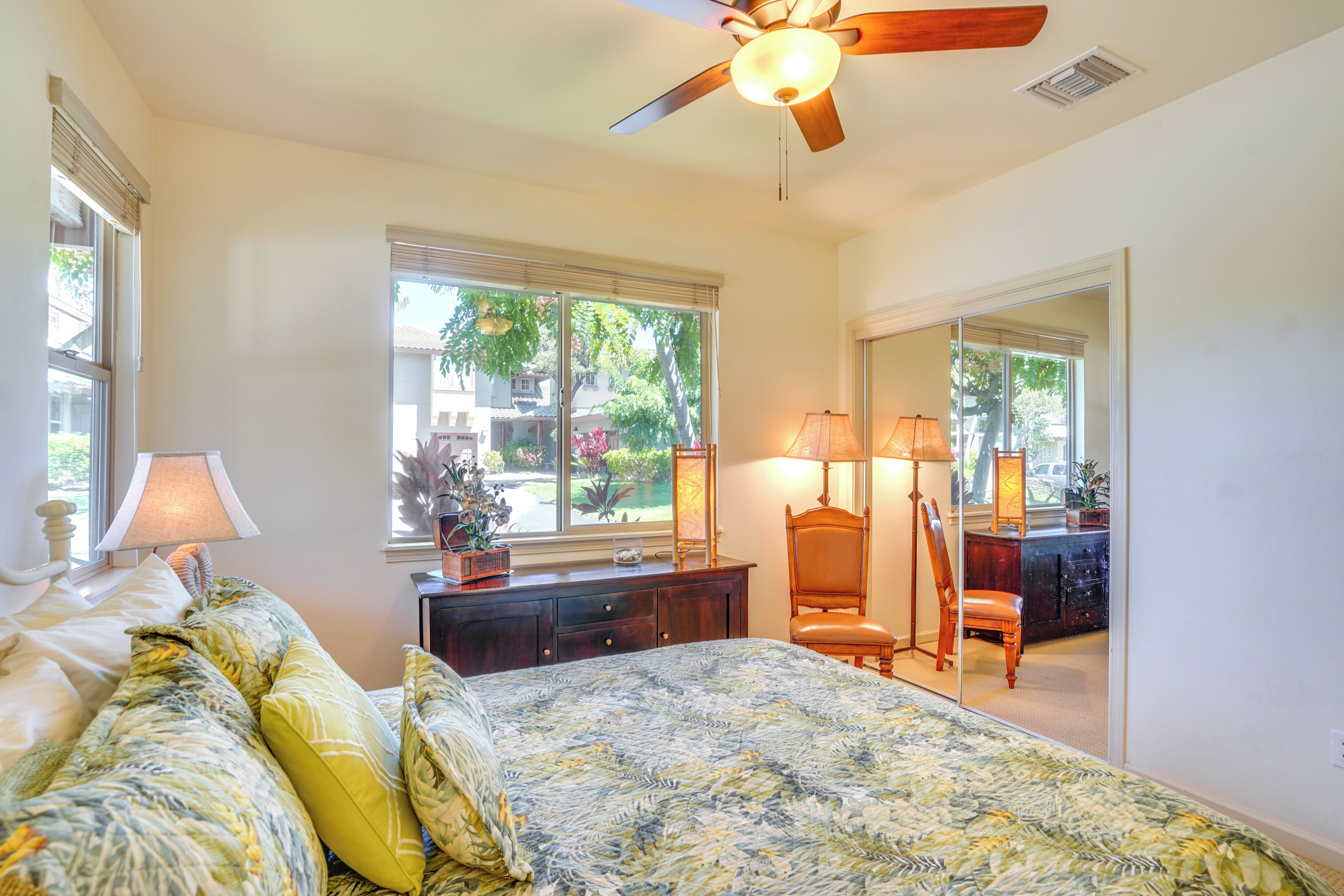 A bedroom with a bed, a ceiling fan, a window with blinds, a dresser, a chair, and a mirror.