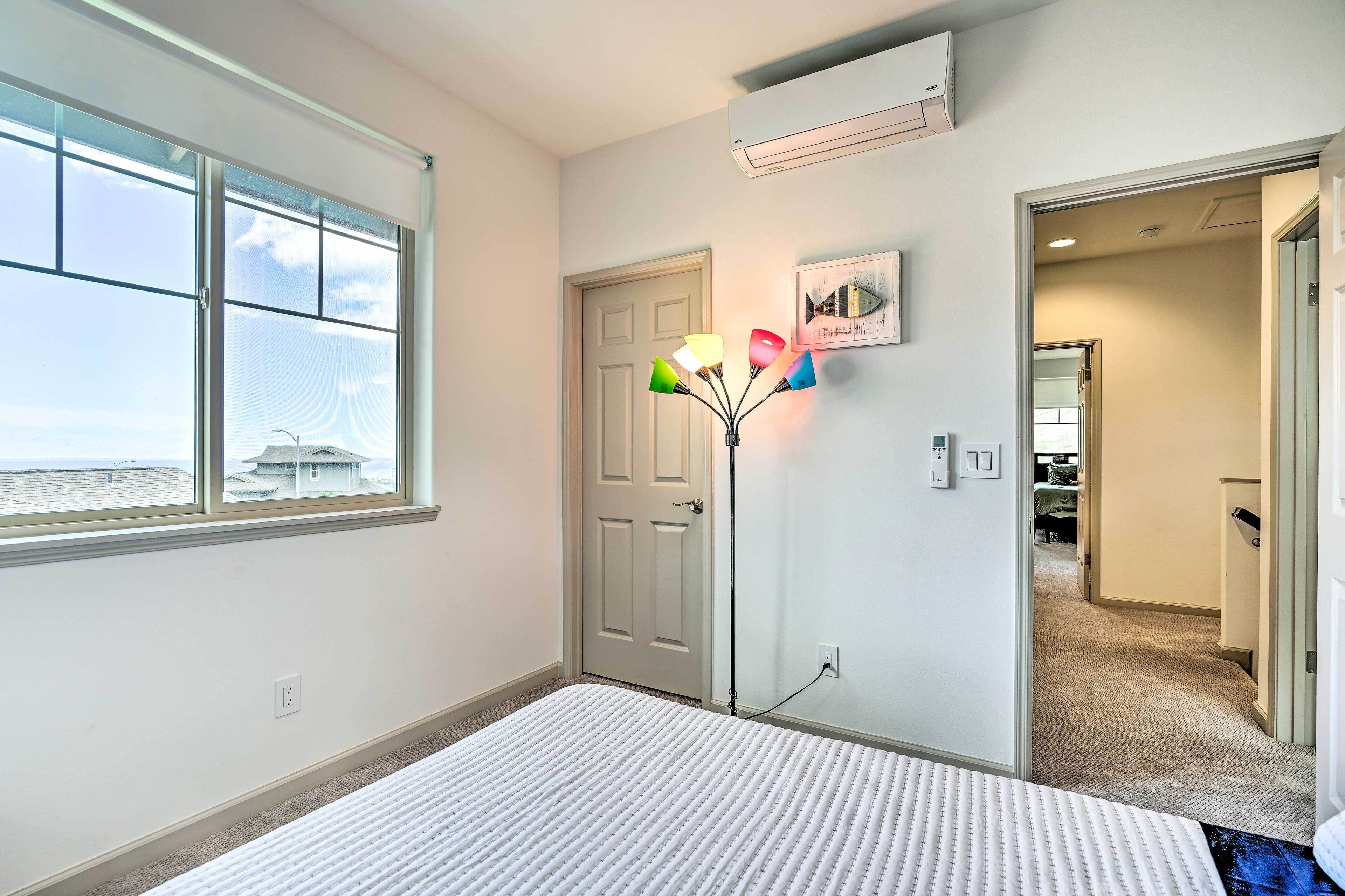A bedroom with a large window, a bed, a floor lamp, and a door leading to another room.