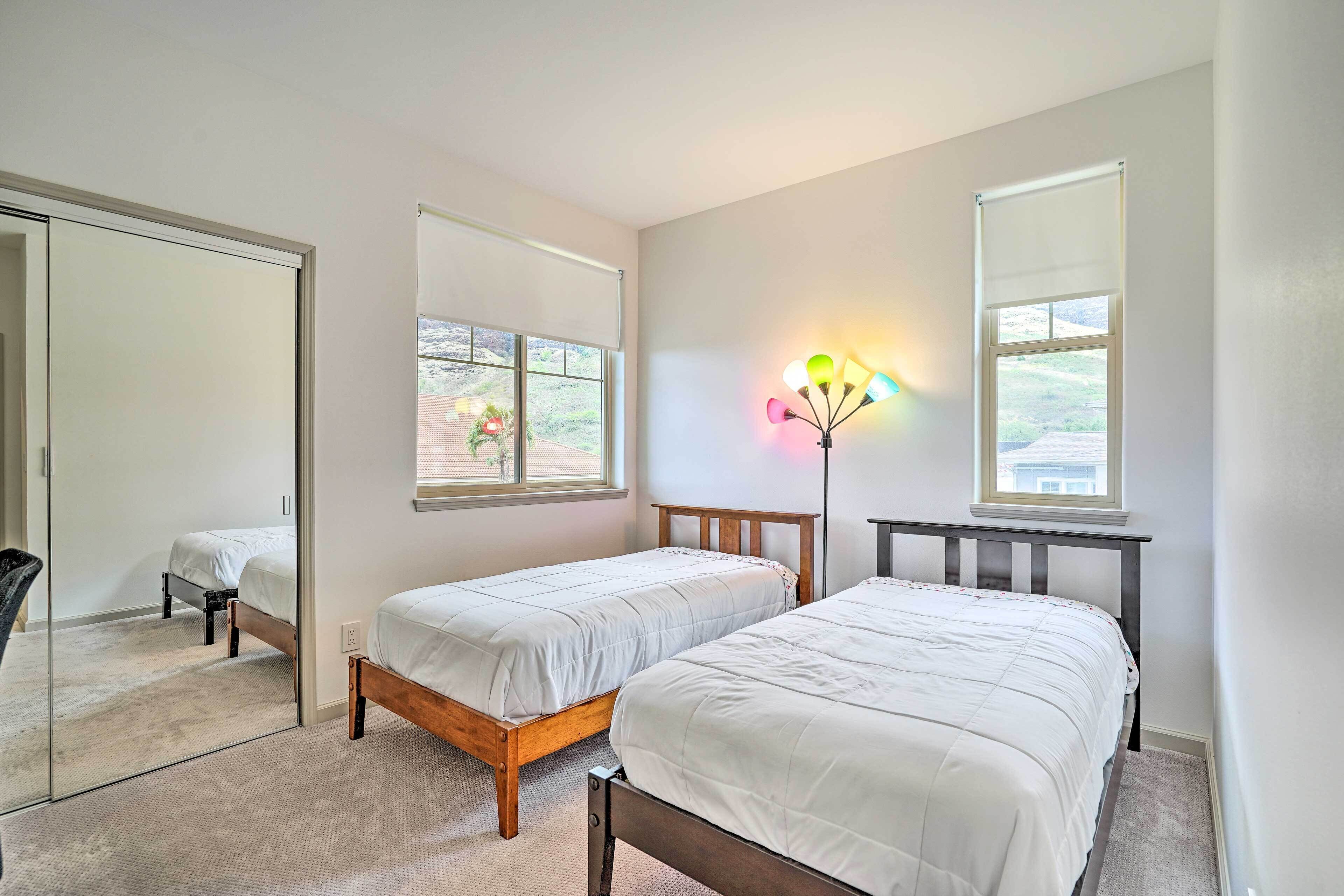 Quarto com duas camas de solteiro, um espelho grande e janela com vista para o verde.