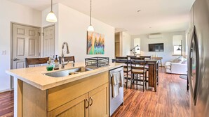 A modern kitchen with a central island, wooden cabinets, a stainless steel sink, and pendant lighting. - Modern Waianae Home w/ Mountain & Valley View (Waianae)