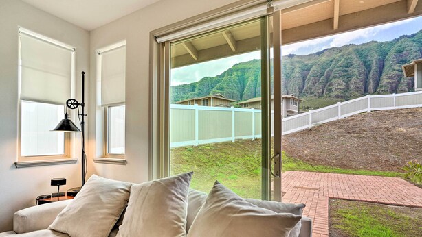 A bedroom with a large window offering a view of a mountainous landscape and a white fence. - Modern Waianae Home w/ Mountain & Valley View (Waianae)