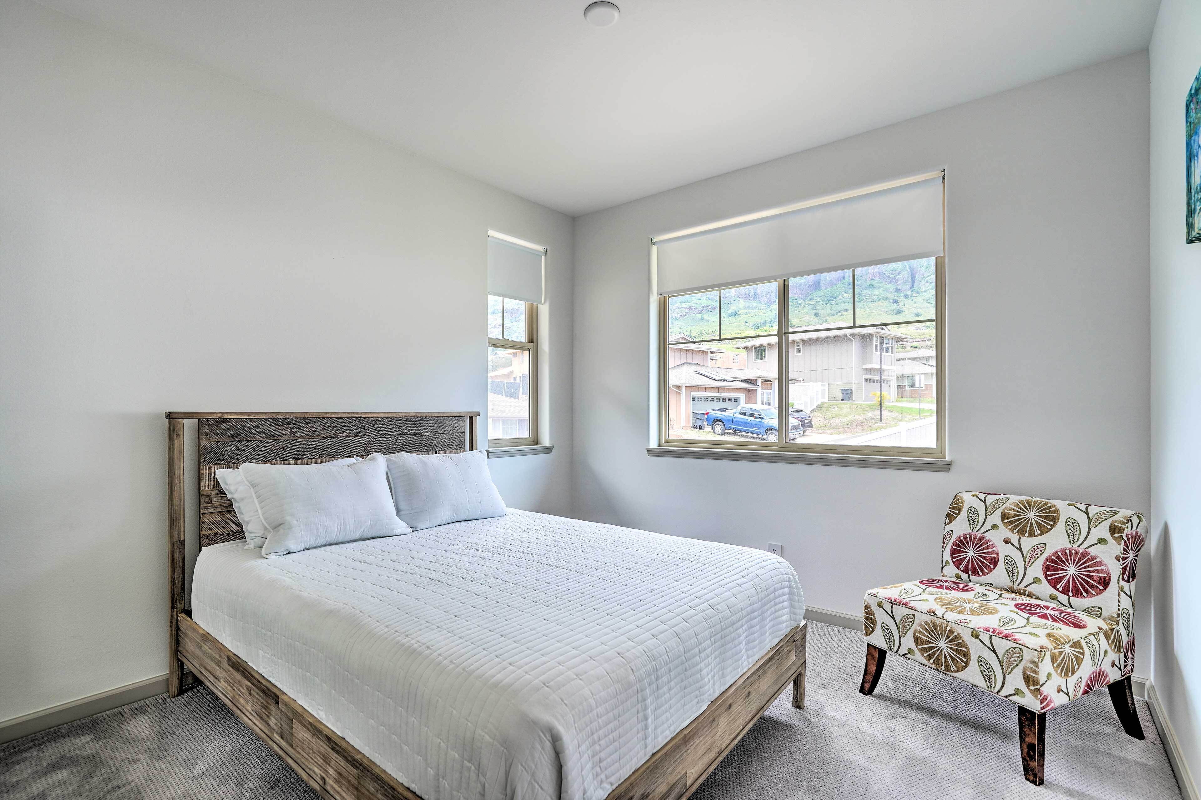 A bedroom with a bed, a chair, and a window with a view of houses.