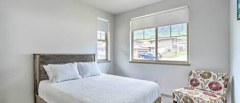A bedroom with a bed, a chair, and a window with a view of houses.