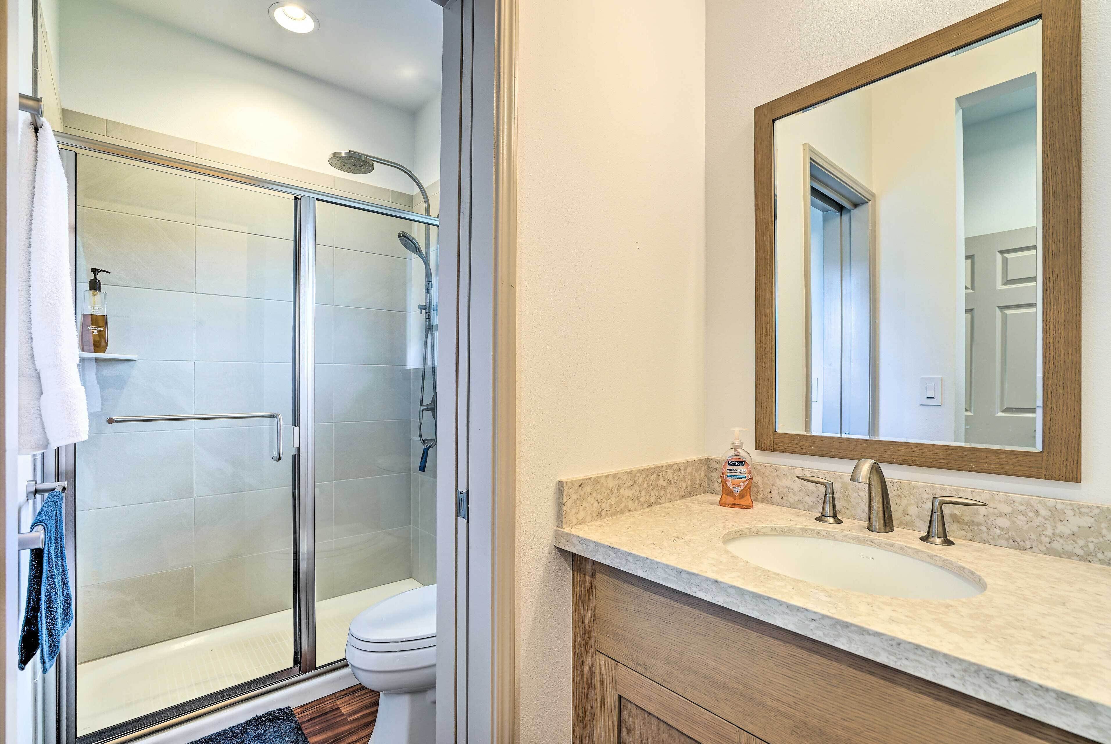 Un baño con cabina de ducha de vidrio, un inodoro, un lavamanos con encimera de mármol y un mueble de tocador de madera.