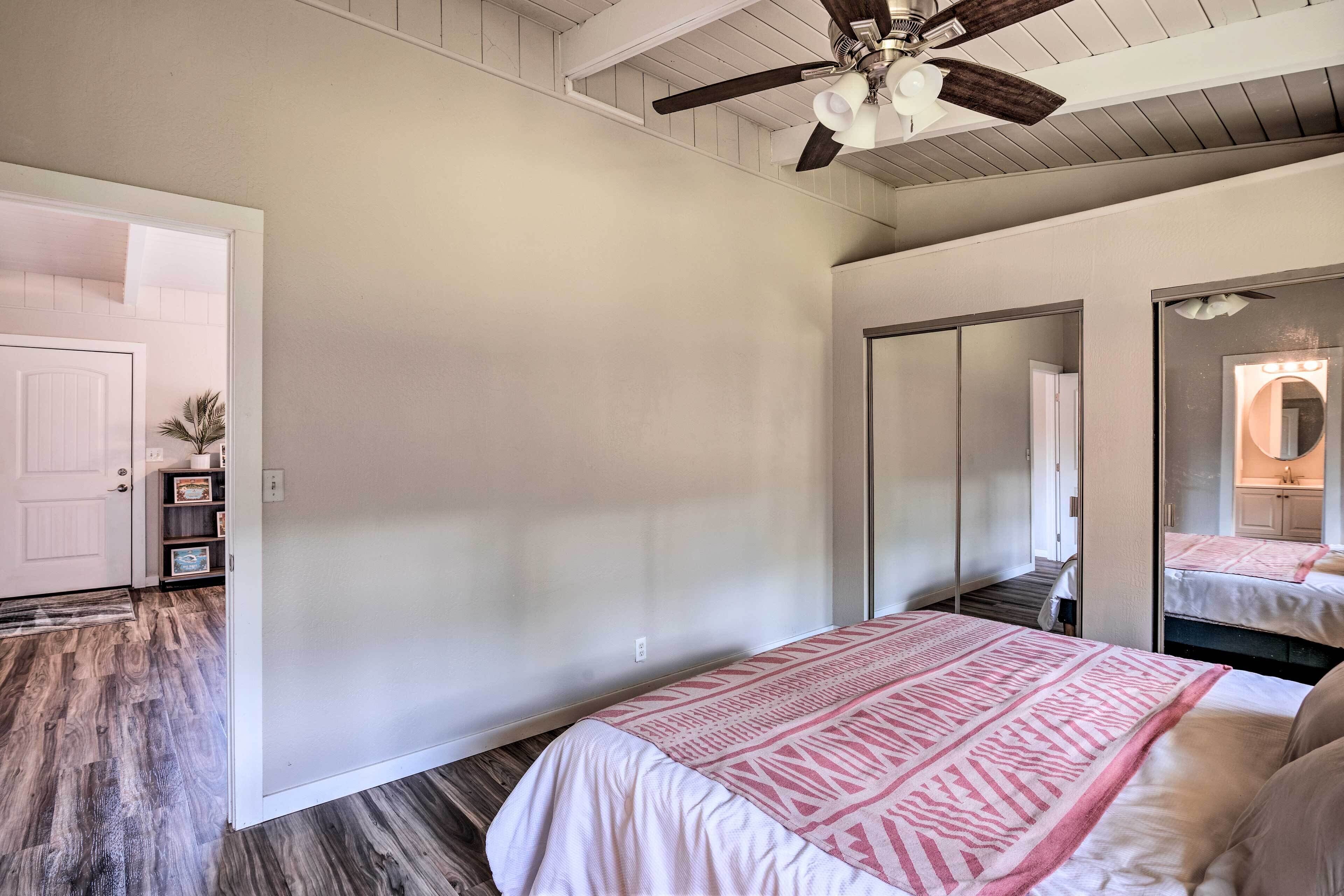 A bedroom with a bed, a ceiling fan, a large mirror, and a door leading to another room.