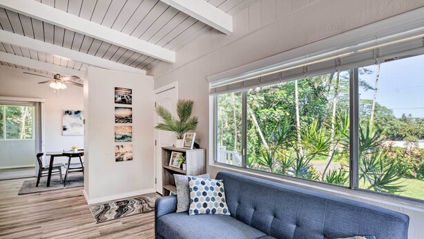 Una sala de estar moderna con un sofá azul, un comedor con mesa y sillas, y un ventanal con vistas a la vegetación.