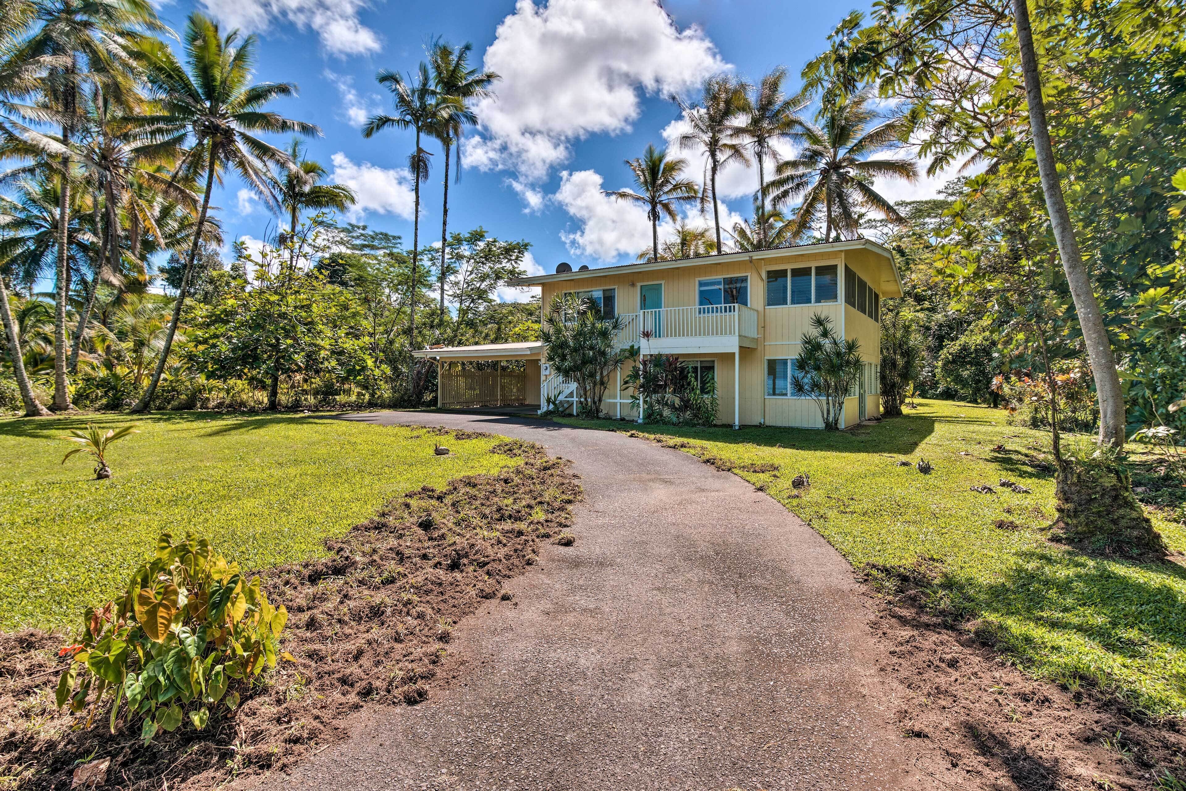 A two-story building with a curved driveway, surrounded by lush greenery and palm trees.
