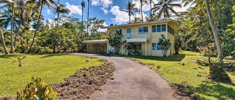 A two-story building with a curved driveway, surrounded by lush greenery and palm trees.