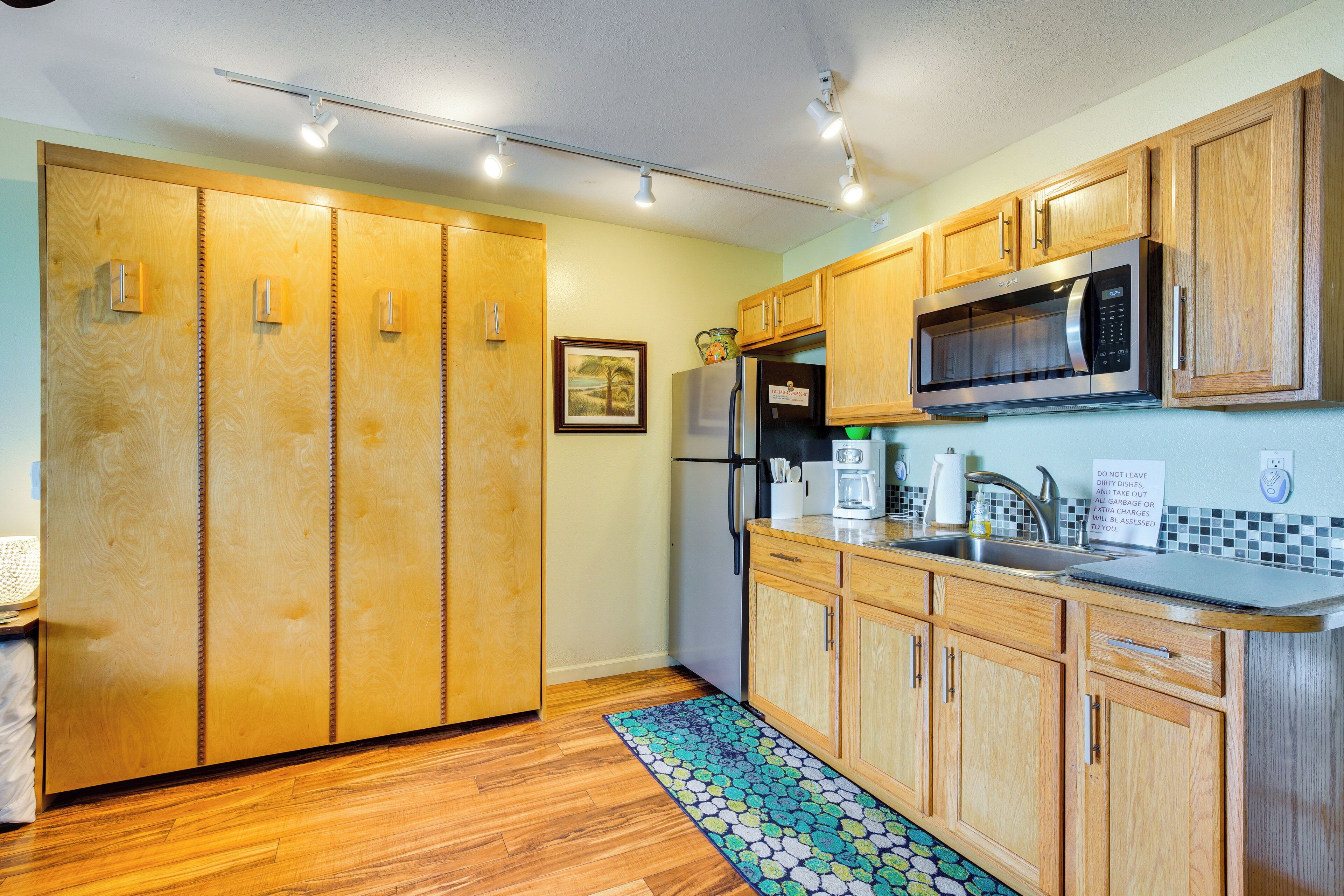 Una cocina con armarios de madera, un microondas de acero inoxidable y un refrigerador.