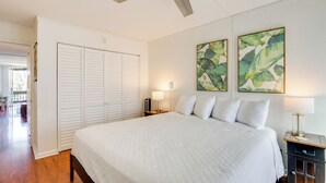 A bedroom with a large bed, a ceiling fan, white walls, and two paintings.