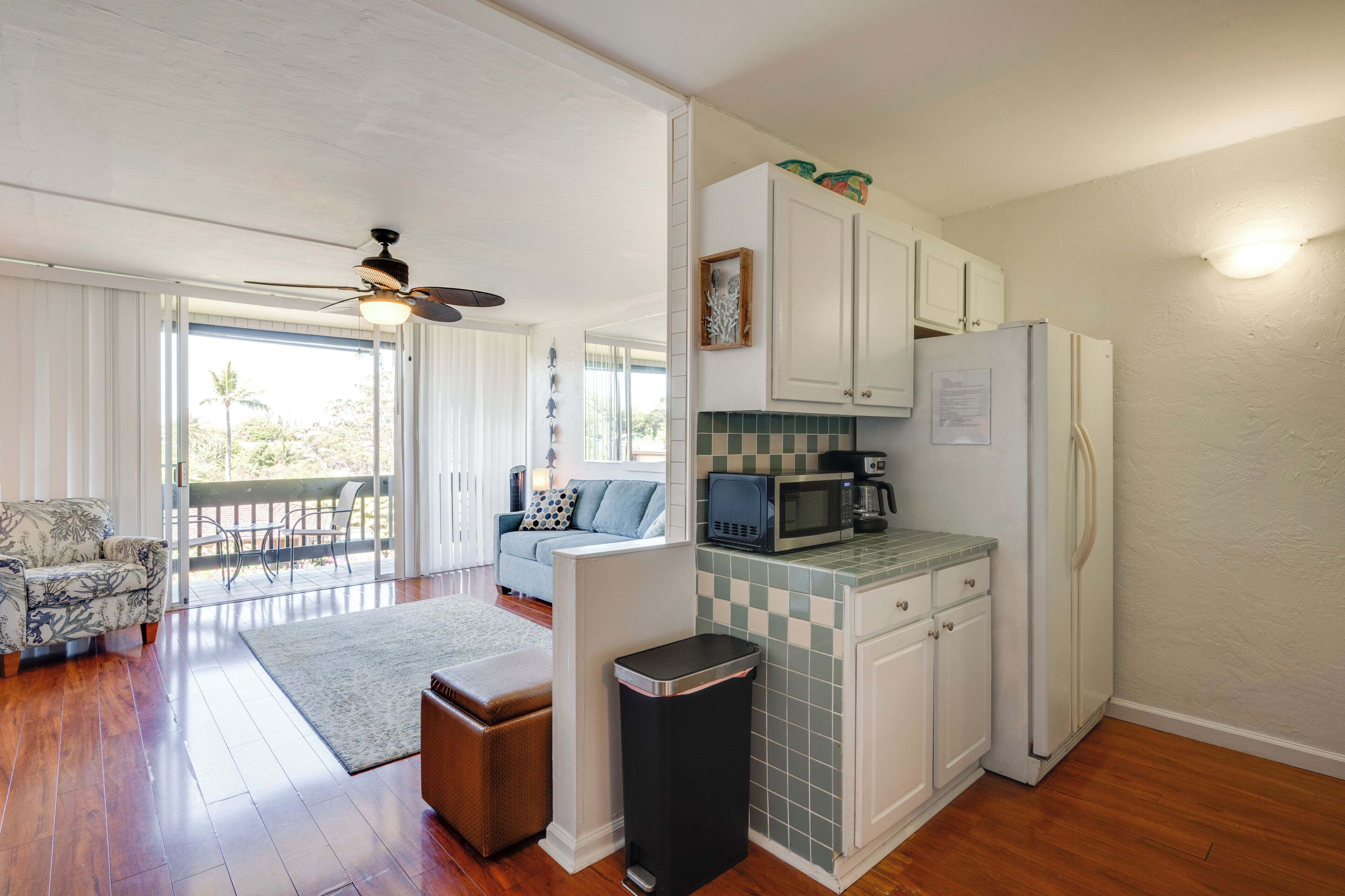 A kitchen with white cabinets, a microwave, and a refrigerator. There is a dining table with chairs and a sofa in the adjacent living area.