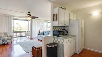 Cozinha com armários brancos, micro-ondas e geladeira. Há uma mesa de jantar com cadeiras e um sofá na sala adjacente.