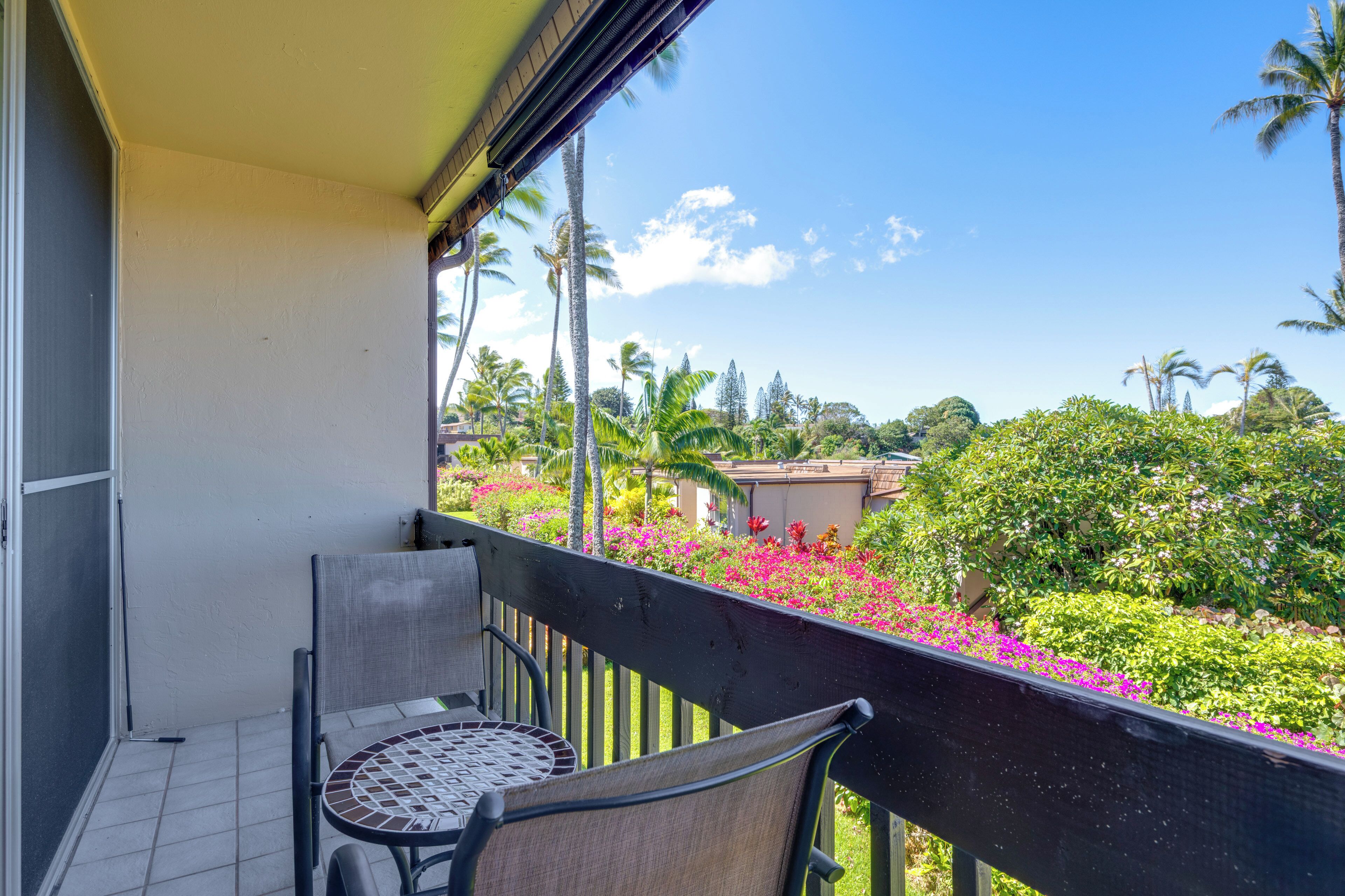 Varanda com mesa e cadeiras, vista para um jardim com diversas plantas e flores.
