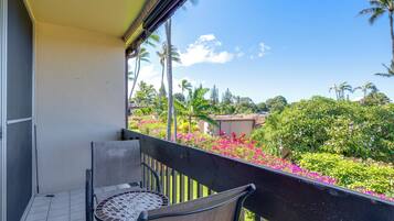 Varanda com mesa e cadeiras, vista para um jardim com diversas plantas e flores.