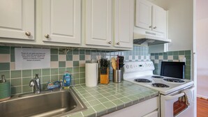 A kitchen with white cabinets, a stainless steel sink, and a stove. There is a sign on the wall advising against washing down the drain.