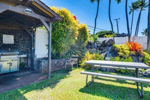 Un patio con una parrilla, una mesa de picnic y un muro de piedra con plantas tropicales.