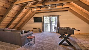 An attic room with a high ceiling, wooden beams, a gray sofa, a foosball table, and a large sliding glass door leading outside. - South Lake Tahoe Cabin ~ 7 Mi to Ski Resort! (South Lake Tahoe)