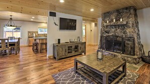A spacious living room with a stone fireplace, wooden flooring, and a dining area with a wooden table and chairs. - South Lake Tahoe Cabin ~ 7 Mi to Ski Resort! (South Lake Tahoe)