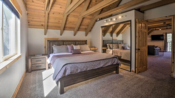 A bedroom with a large bed, wooden ceiling beams, a walk-in closet, and a TV mounted on the wall. - South Lake Tahoe Cabin ~ 7 Mi to Ski Resort! (South Lake Tahoe)