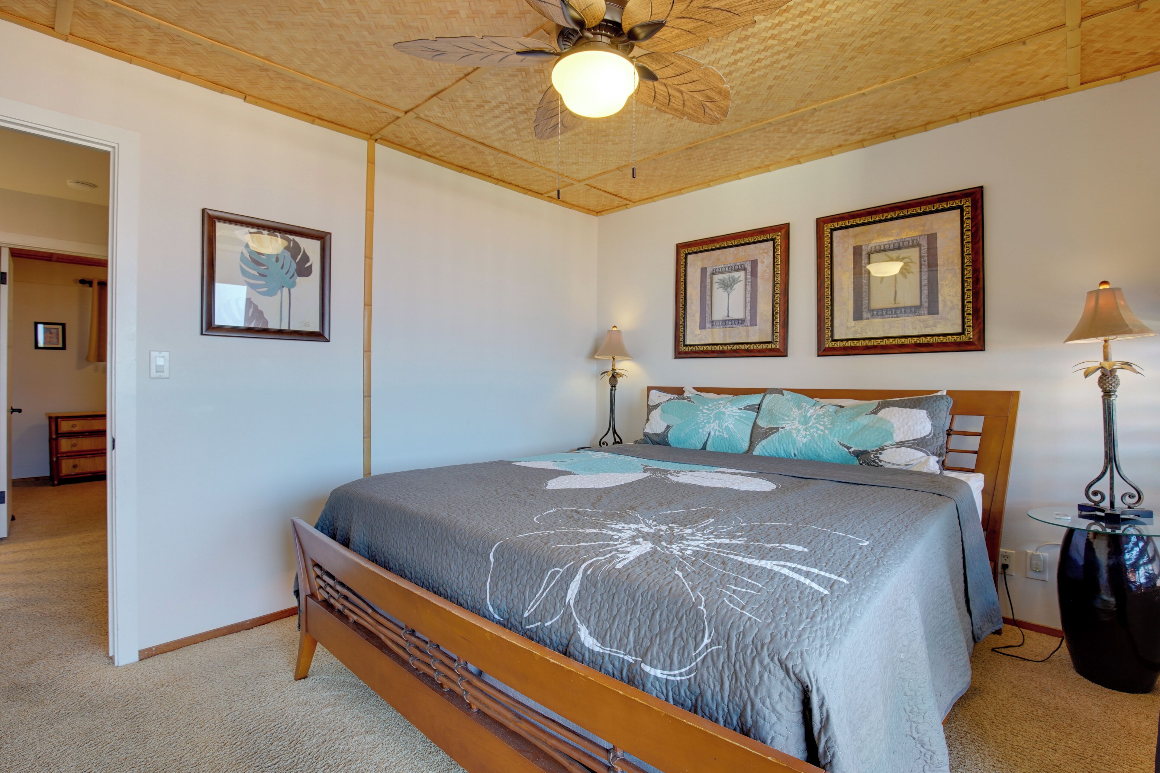Une chambre avec un lit en bois, un ventilateur de plafond et des œuvres d’art encadrées accrochées aux murs.