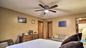 Une chambre avec un grand lit, un ventilateur de plafond, des meubles en bois et une porte donnant sur une autre pièce.