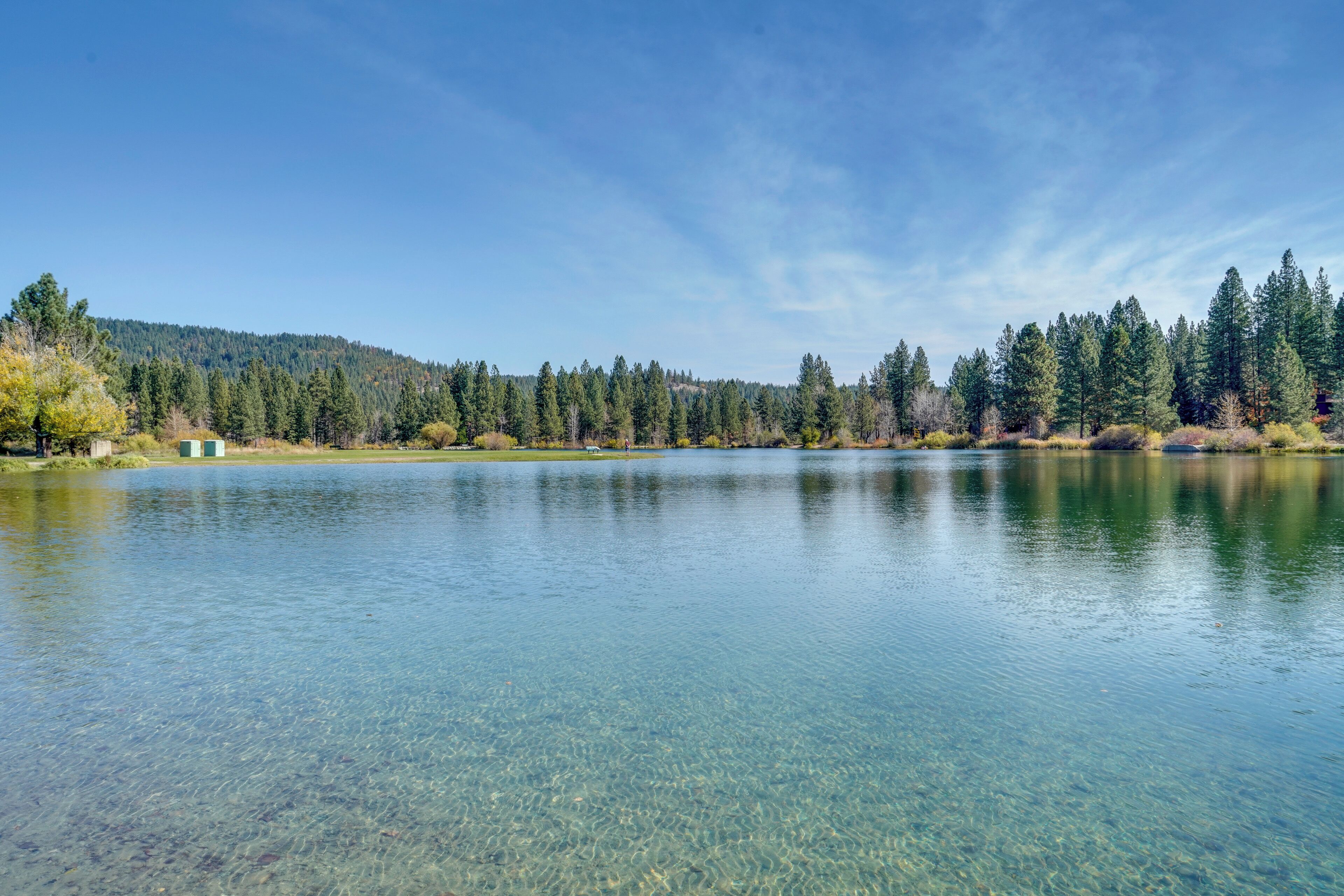 A clear lake with a forested hillside in the background.