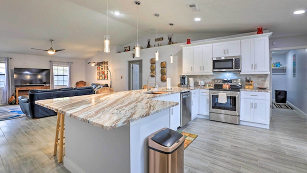 Una cocina moderna con gabinetes blancos, electrodomésticos de acero inoxidable y una isla con encimera de mármol.