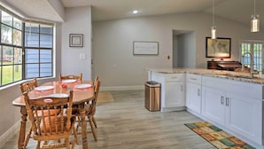Una cocina moderna con una mesa de comedor para cuatro personas, armarios blancos y un amplio ventanal que proporciona luz natural.