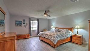 Un dormitorio con cama de madera, mesitas de noche, ventilador de techo y ventana con cortinas.