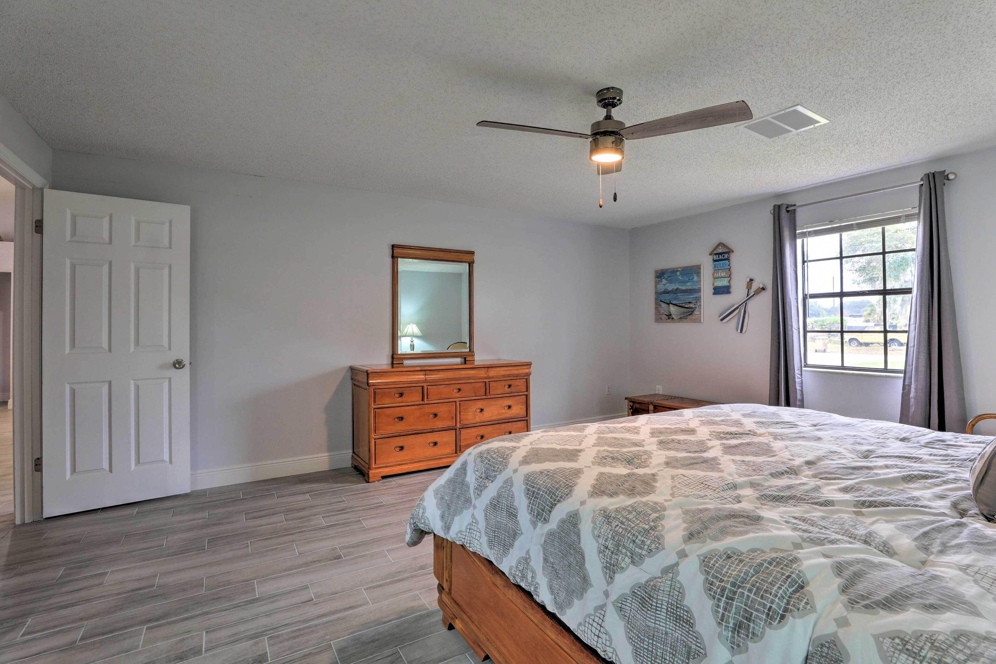 A bedroom with a bed, dresser, ceiling fan, and a window with curtains.