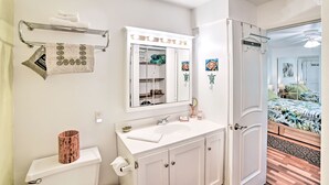 A bathroom with a toilet, sink, vanity, and a mirror with lights above. - Waikoloa Village Home in Resort Golf Community (Waikoloa)