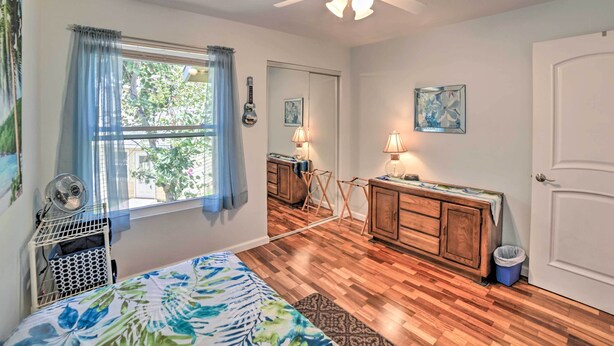 A bedroom with a bed, a ceiling fan, a window with curtains, a wooden dresser, and a small table with a lamp. - Waikoloa Village Home in Resort Golf Community (Waikoloa)
