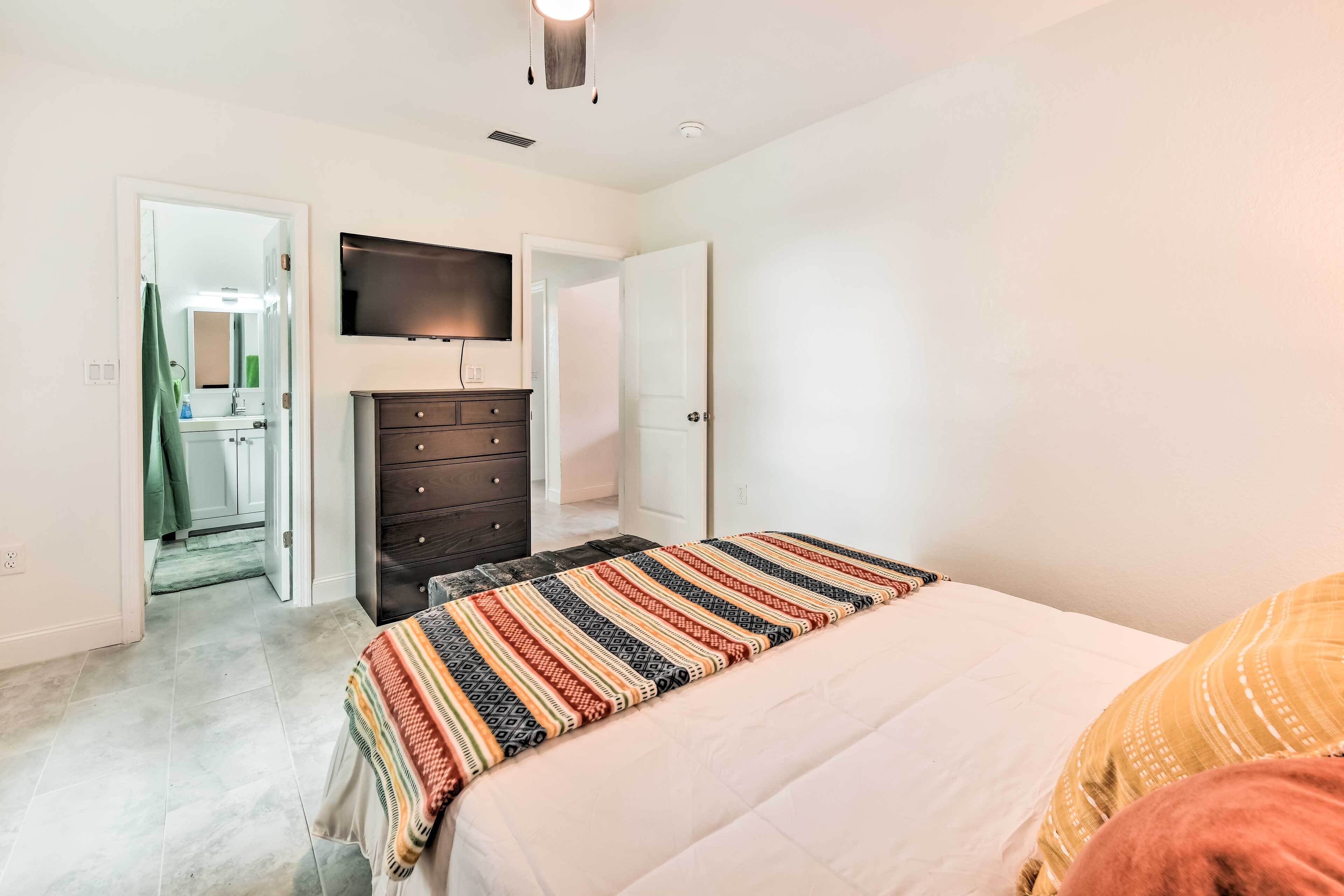 A bedroom with a bed, a dresser, a television, and a bathroom visible through an open door.