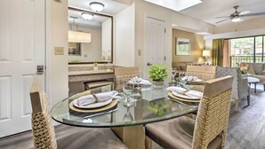 Un comedor con una mesa de vidrio, sillas acolchadas y vistas al salón contiguo.