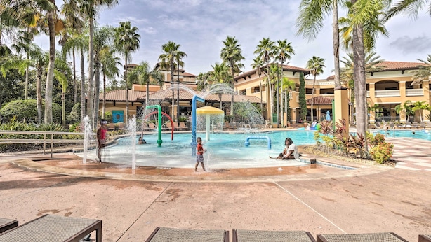 Zona de piscina en un complejo turístico, con palmeras, una estructura de juegos acuáticos y sillones de descanso.
