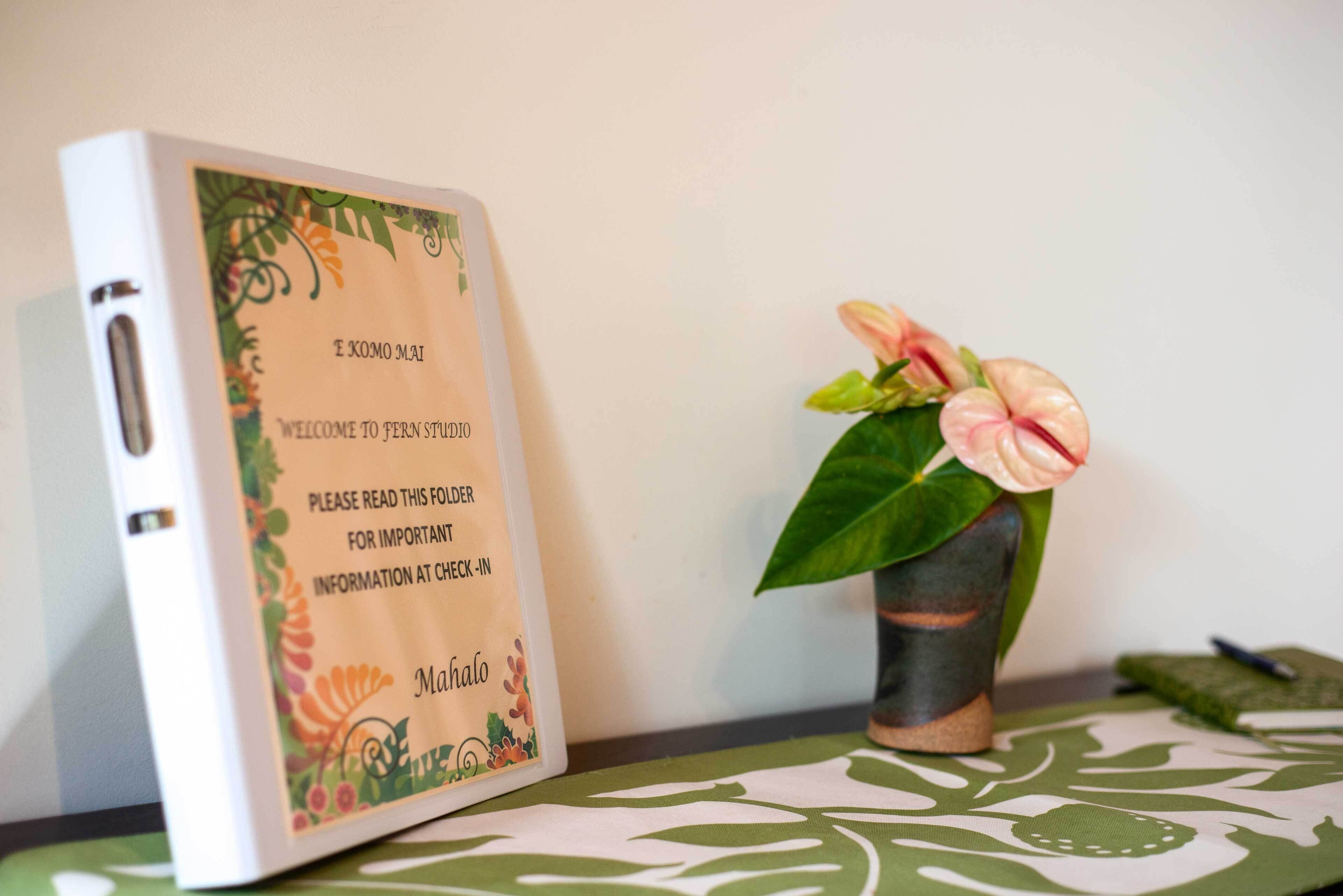 Un cuaderno con diseño floral y texto, junto a una maceta con flores rosadas.