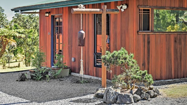 Een houten gebouw met een groen dak, een houten veranda en een kleine tuin met stenen en planten.